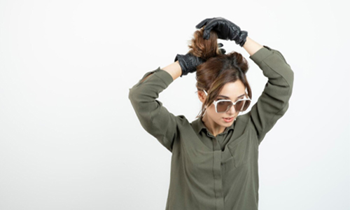 Woman tying her hair into a casual ponytail look reflecting the messy girl aesthetic.