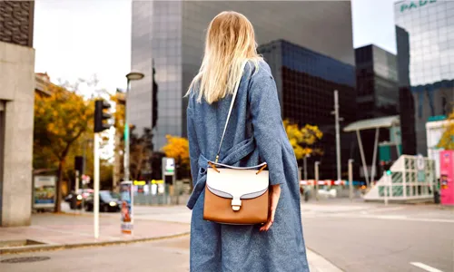 Woman carrying a stylish handbag with a blue coat on a city street