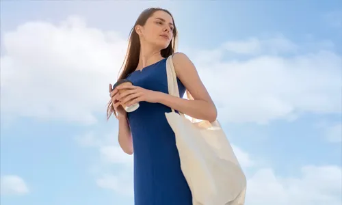 Woman carrying a fabric tote bag outdoors bright sky background