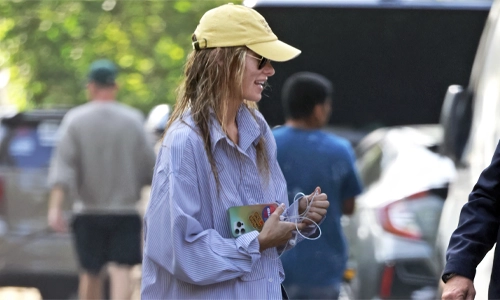 Olivia Wilde wearing an oversized striped shirt, cap, and sunglasses in a casual street style look