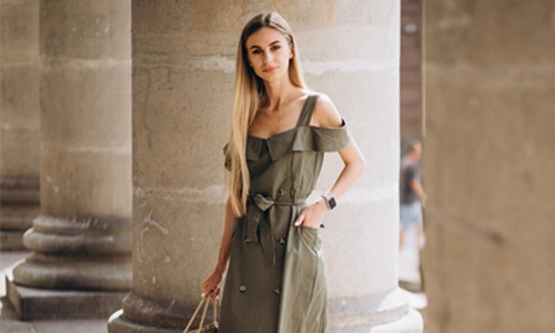 Young woman in green color summer outfit paired with nude shoes by an old building
